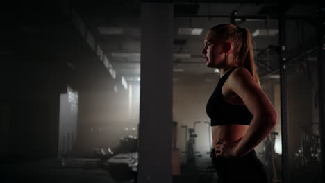 Young-woman-resting-after-her-workout-and-looking-down.-Female-athlete-taking-rest-after-fitness-training-in-dark-gym